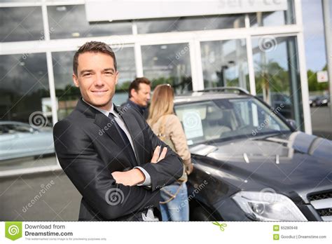Portrait Of Car Salesman With Clients In The Back Stock Photo Image