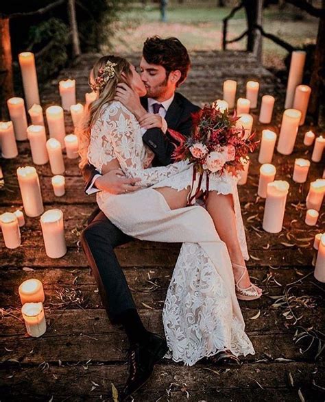 A Bride And Groom Are Sitting On A Bench In Front Of Candles With Their Faces Close To Each Other