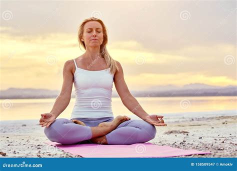 Middle Aged Woman Seated In Lotus Pose Doing Meditation On Nature Stock