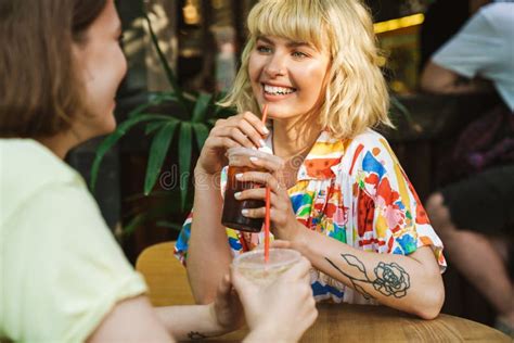 Image Of Two Women Laughing And Drinking Soda While Sitting At Table