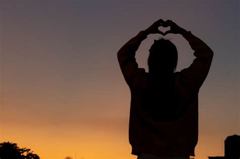 A Silhouette Of A Young Woman Raising Her Hands Above Her Head To Represent A Heart Symbol