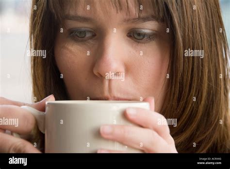 A Young Woman Sips Her Coffee And Talks On The Phone As She Relaxes In