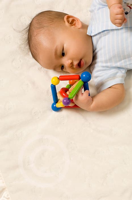 By around four to six months, your baby. 4 month old baby boy holding and inspecting toy Asian ...