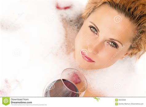 Relaxing Sensual Caucasian Blond Female In Foamy Bathtub Holding A Glass Of Red Wine Stock