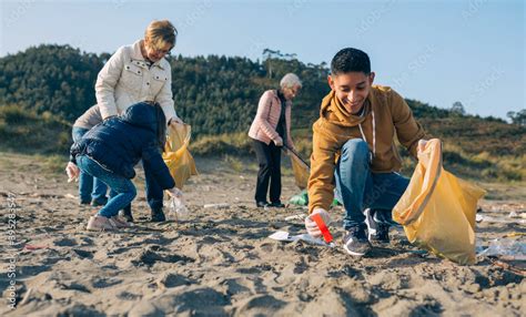 Young Man Picking Up Trash With Group Of Volunteers On The Beach Stock