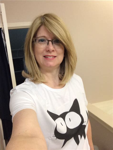 a woman with glasses is taking a selfie in front of a mirror wearing a cat t shirt