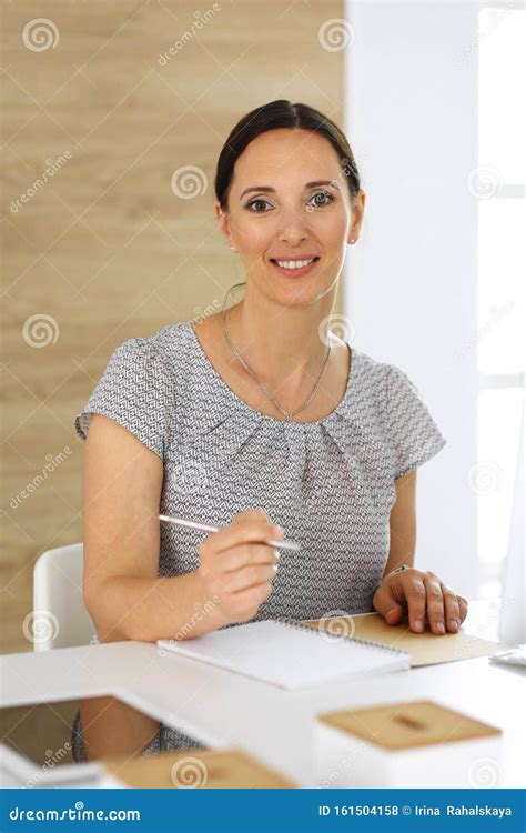 cheerful smiling business woman working with pc computer while sitting at the desk in modern