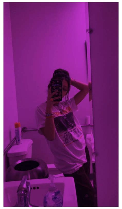 A Woman Taking A Selfie In A Bathroom Mirror With Purple Light Behind Her