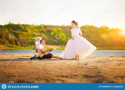 Romantic Wedding Couple At Sunset On The Shore With A Guitar. The Bride And Groom Near The Shore ...