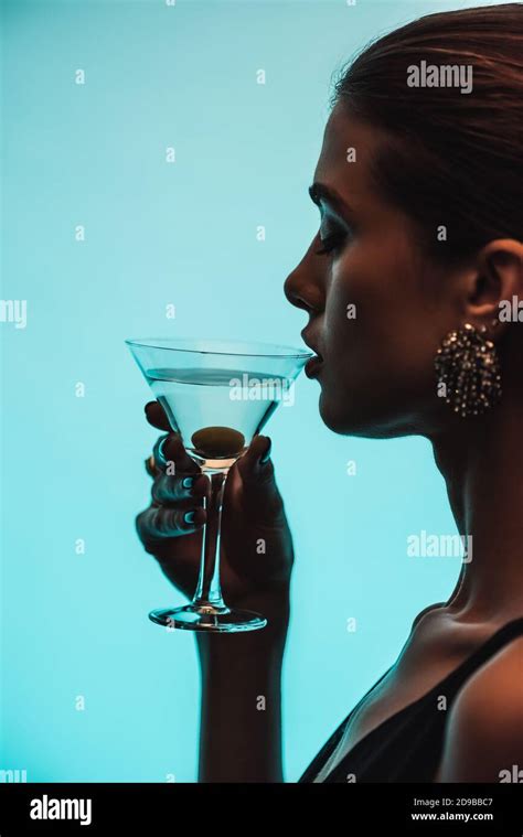 Side View Of Woman Holding Glass And Drinking Martini Isolated On Blue
