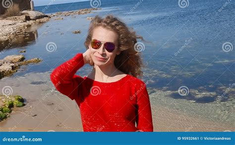 Close Up Portrait Of Woman Running Hand Through Curly Hair Blowing In Wind By Sea On Beach