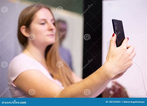 A Young Blondie Lady Holds In Hand Black Smartphone Looks Into It Doing