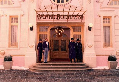 Two Men In Suits Stand Outside The Grand Budapest Hotel Entrance With Their Hands In Their Pockets