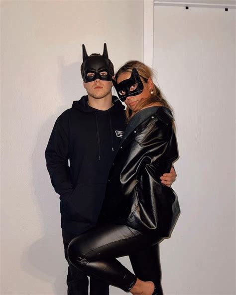 Two People Dressed Up As Batman And Catwoman Standing Next To Each Other In Front Of A White Wall