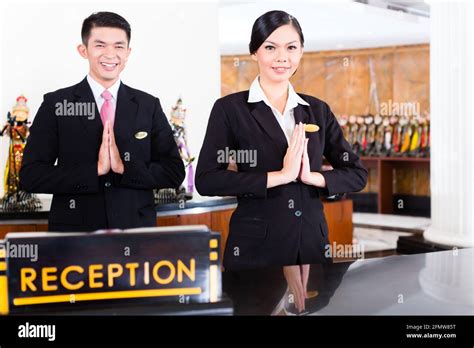 Chinese Asian Reception Team At Luxury Hotel Front Desk Welcoming Guests With Typical Gesture A