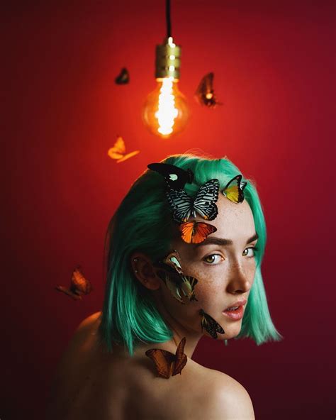A Woman With Green Hair And Butterflies On Her Head In Front Of A Red