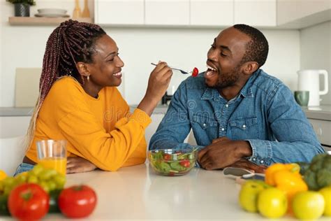 romantic african american couple eating healthy salad in kitchen happy