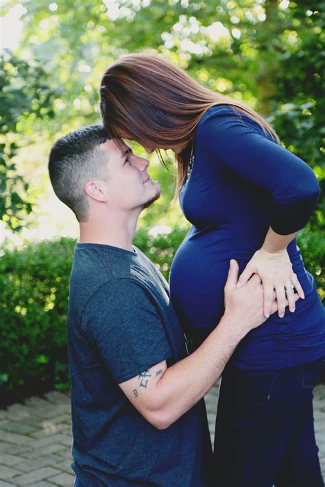 A Pregnant Couple Kissing While Standing Next To Each Other