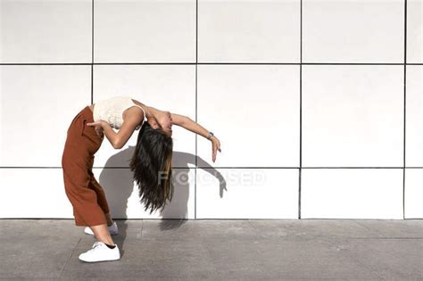 Young Woman Bending Backwards With Hand On Hip Against Wall During