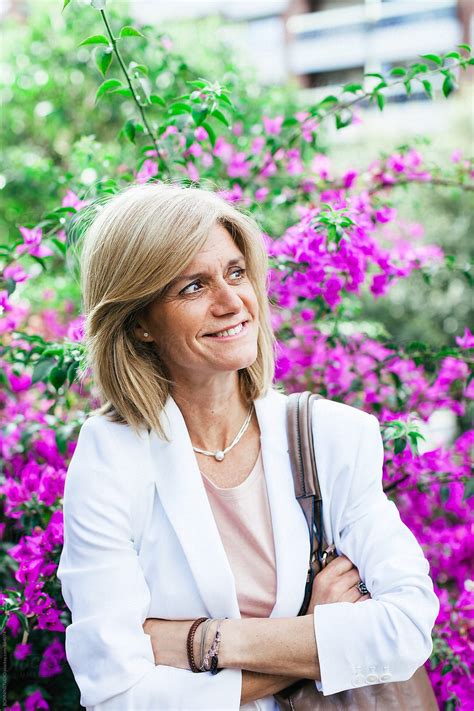 Portrait Of A Mature Businesswoman Standing In Front Of Purple Flowers Del Colaborador De