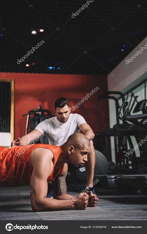 Attentive Trainer Instructing African American Sportsman Doing Plank