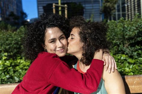 pareja de lesbianas sonrientes que abrazan y que se relajan en un banco del parque imagen de