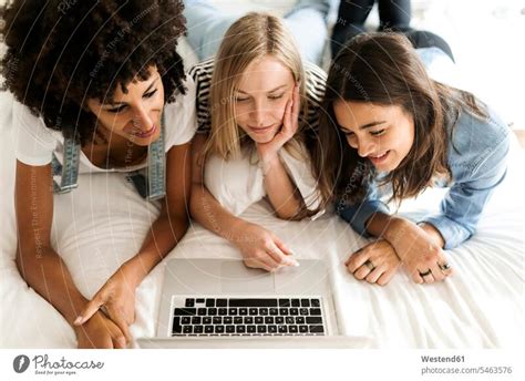 Three Girlfriends Lying On Bed Sharing Laptop A Royalty Free Stock