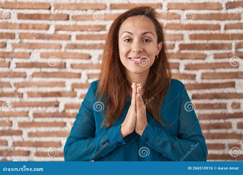 Brunette Woman Standing Over Bricks Wall Praying With Hands Together