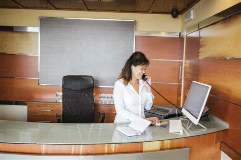 Female Receptionist Smiling And Talking On Telephone At Reception Desk