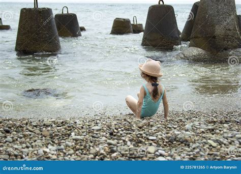 A Little Girl In A Swimsuit And A Hat Runs On The Seashore The Child