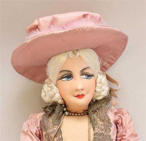 A Doll Wearing A Pink Hat And Dress With Pearls On Its Head Is Posed
