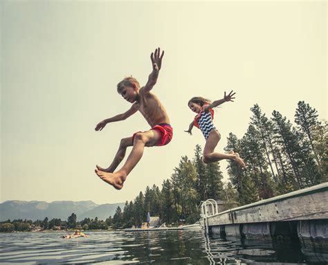 Kids Jumping Off The Dock Into A Beautiful Mountain Lake Having Fun On