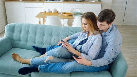 Guy And Girl Sit On Sofa Surfing Internet In Smartphones Stock Image