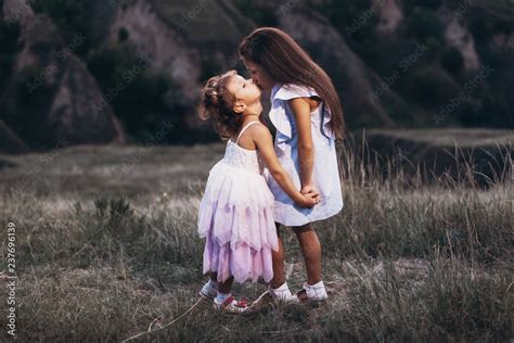 Cute Little Sisters In White Dresses Hugging And Kissing Foto De Stock