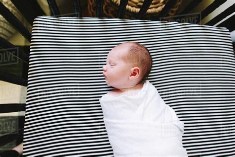 A newborn baby boy sleeping in a swaddle in his crib - Stock Photo 