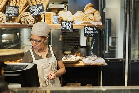 A Man In An Apron Is Working Behind The Counter At A Bakery With Breads