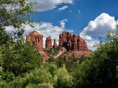 The Red Rock Formations Are Surrounded By Trees And Bushes On A Sunny
