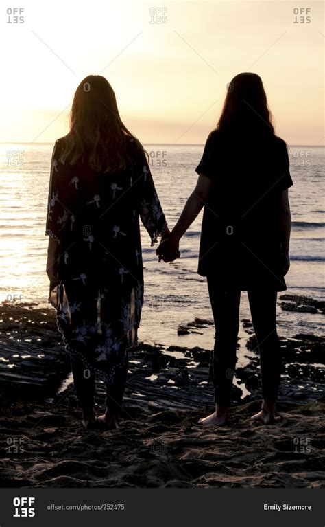 Silhouette Of Two Young Women Holding Hands On The Beach At Dusk Stock