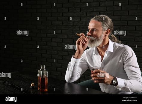 Senior Man Drinking Whiskey And Smoking Cigar On Dark Background Stock