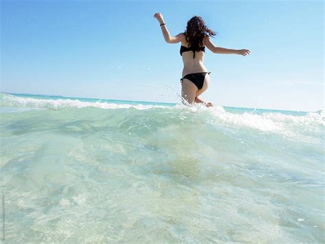 Woman In A Black Bikini Running Through The Sea Water By Stocksy