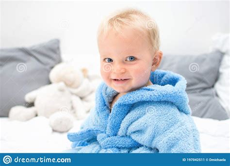 Ten Month Blond Baby Boy Crawling On Bed In Blue Bathrobe White