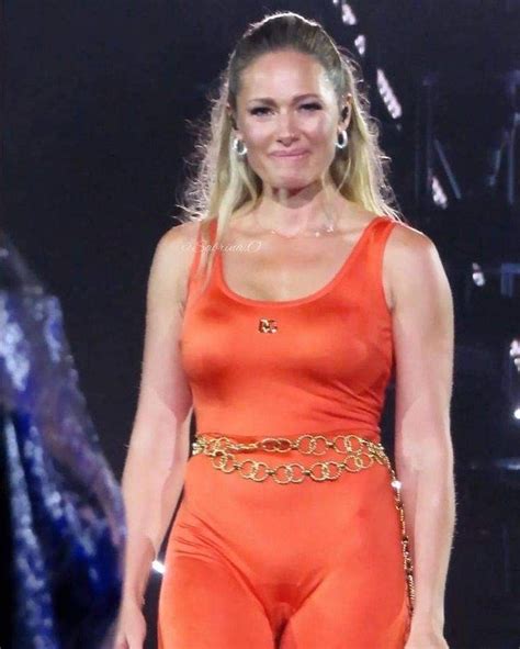 A Woman In An Orange Jumpsuit Walking Down The Runway With Her Hand On