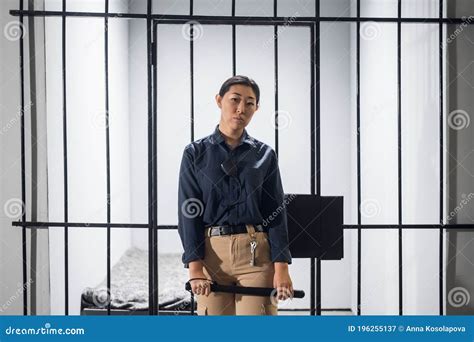 A Young Prison Guard Poses In Front Of Prison Bars In Uniform In A