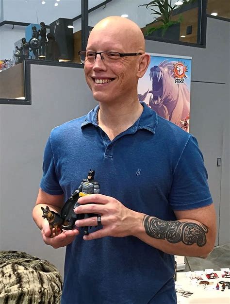 A Bald Man Holding A Small Toy In His Right Hand And Smiling At The Camera