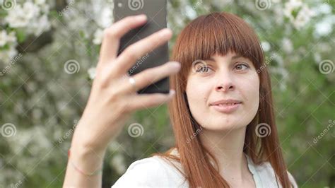 a girl makes selfie in the garden an attractive red haired woman smiles making selfi using a