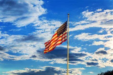 American Flag Flying In The Breeze Against Blue Sky With White Clouds
