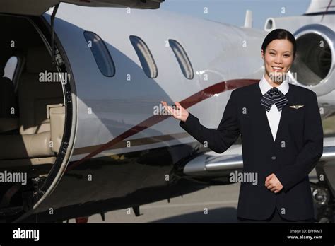 Female Asian Mid Adult Flight Attendant In Front Of Private Jet Stock