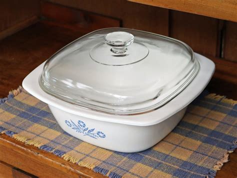 A White Casserole Dish With A Glass Lid On A Blue And Yellow Placemat