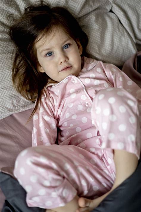 Little Dark Haired Girl In Pink Pajamas Lies On A Cozy Soft Bed Good Morning Stock Image