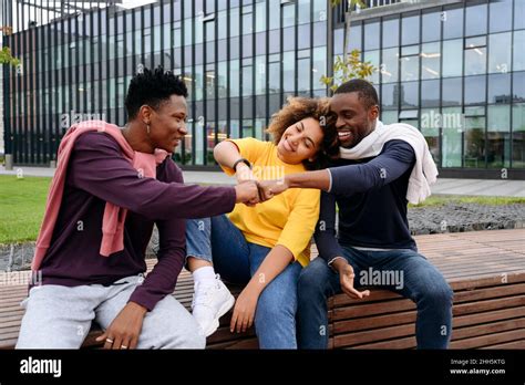 Happy Friends Doing Fist Bump Sitting On Bench Stock Photo Alamy
